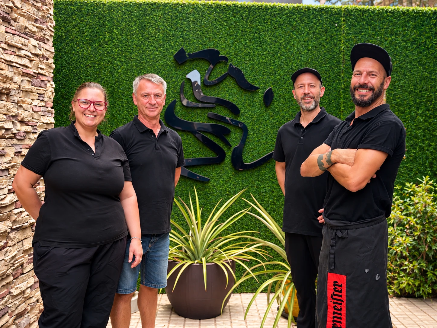 Four Eulenspiegel Tenerife team members in front of the green wall and restaurant logo